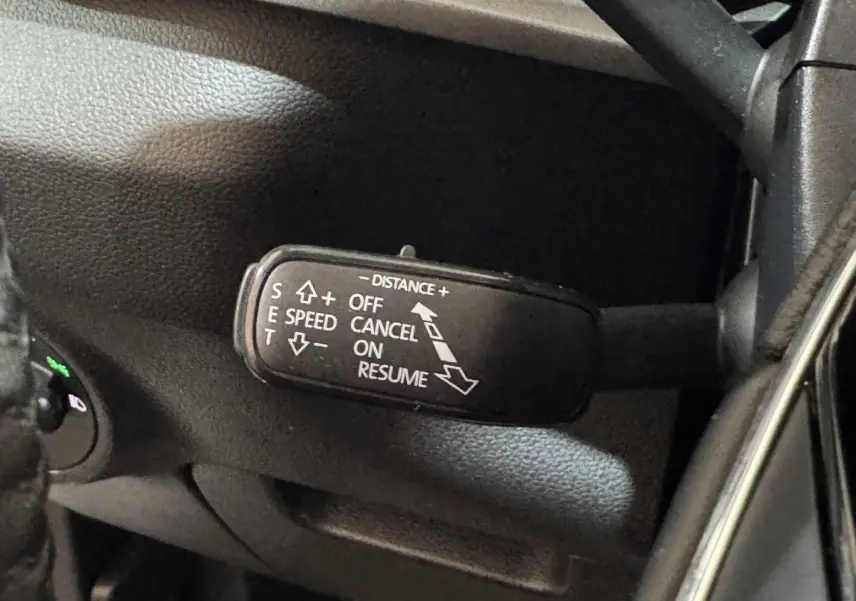 Gros plan sur la commande de régulateur de vitesse au volant d’un Skoda Karoq blanc, intérieur noir.