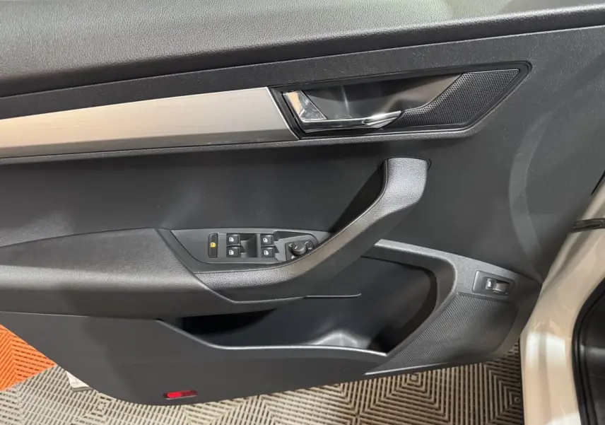Vue intérieure du panneau de porte côté conducteur du Skoda Karoq blanc, avec commandes électriques et poignée noire.