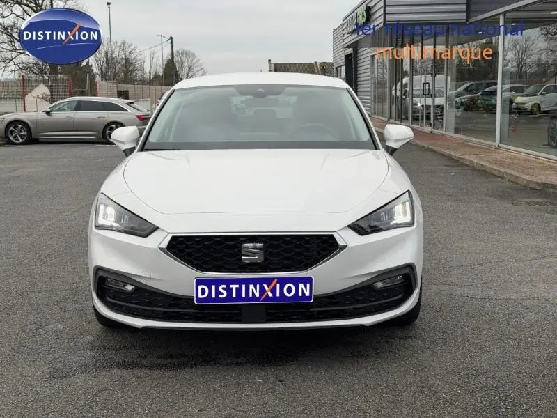 Vue frontale d'une SEAT LEON 2.0 TDI blanche, avec calandre noire et phares LED allumés, sur parking extérieur.