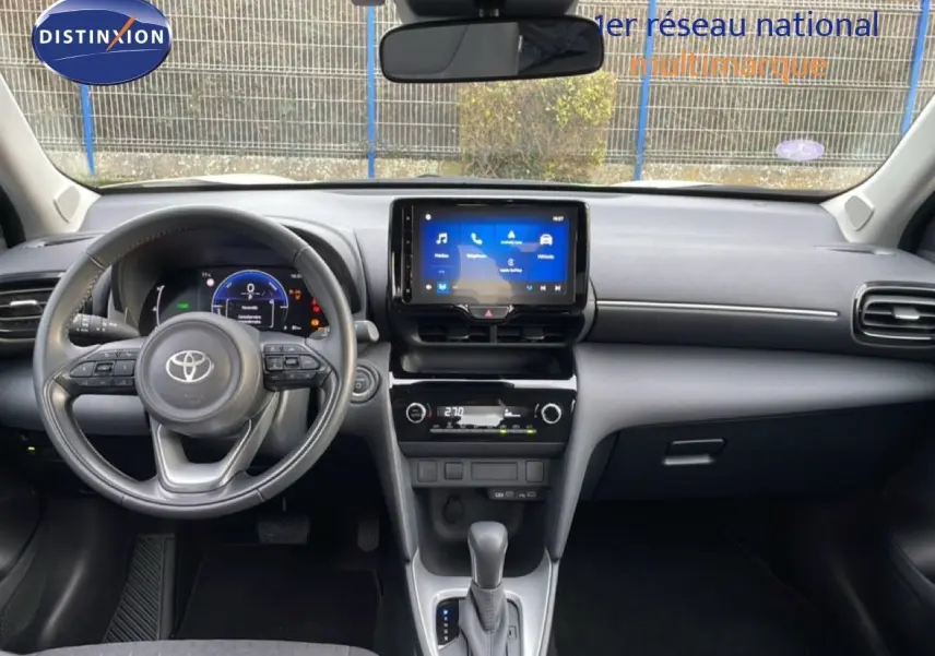 Vue intérieure frontale du tableau de bord et volant du Toyota Yaris Cross blanc, avec écran tactile central allumé.