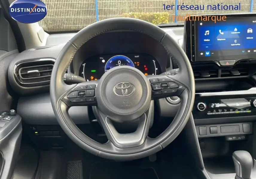 Vue intérieure centrée sur le volant et le tableau de bord du Toyota Yaris Cross blanc pur, avec écran tactile et commandes intégrées.