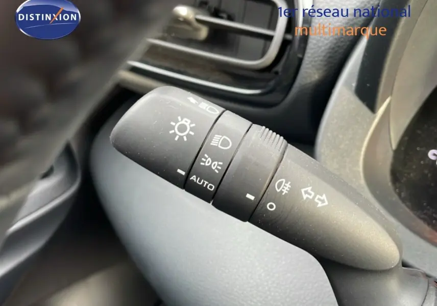 Gros plan sur la commande des phares et clignotants à gauche du volant dans l’habitacle d’une Toyota Yaris Cross blanche.