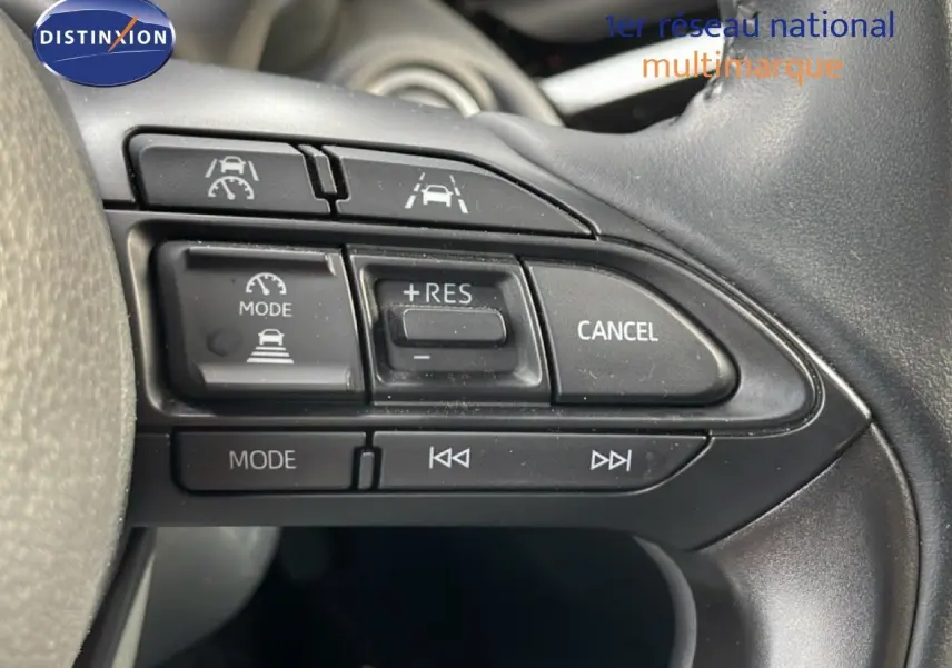 Gros plan sur les commandes au volant noir de la Toyota Yaris Cross 2024, boutons de régulateur de vitesse et multimédia visibles.