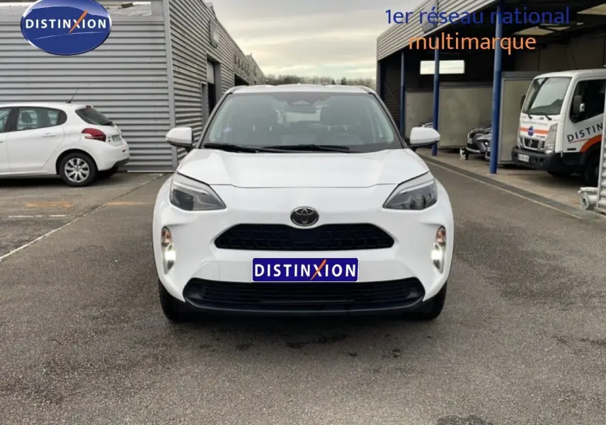 Vue de face d'une Toyota Yaris Cross 1.5 Hybrid blanche, avec calandre noire et phares LED allumés.