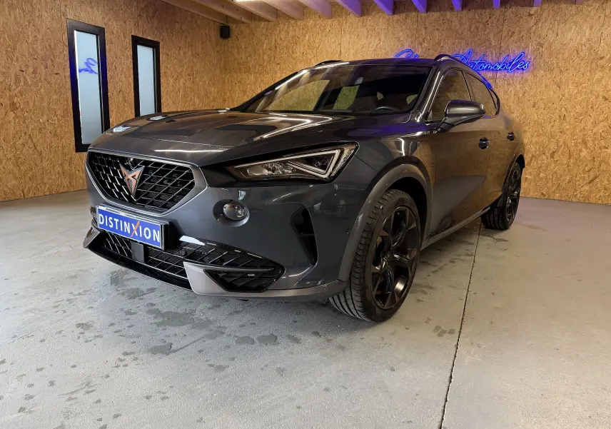 Vue 3/4 avant droite du CUPRA Formentor gris clair 2023 avec jantes noires et détails cuivrés, dans un showroom intérieur.