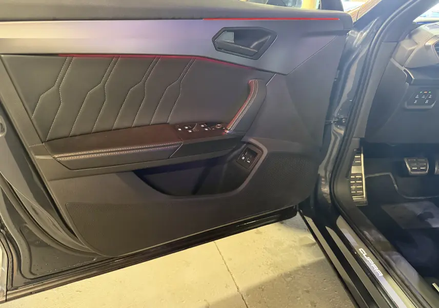 Vue intérieure côté gauche de la porte avant d'une CUPRA Formentor gris clair avec surpiqûres et commandes électriques.