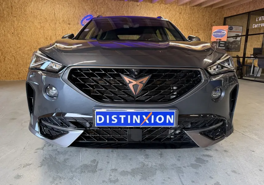 Vue frontale d’un CUPRA Formentor gris clair 2023 avec calandre noire et logo cuivré, en intérieur showroom.