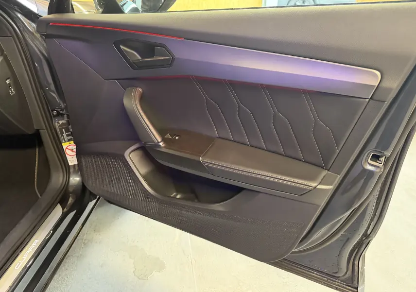 Vue intérieure de la porte avant gauche de la CUPRA Formentor gris clair, avec surpiqûres apparentes et poignée en cuir noir.