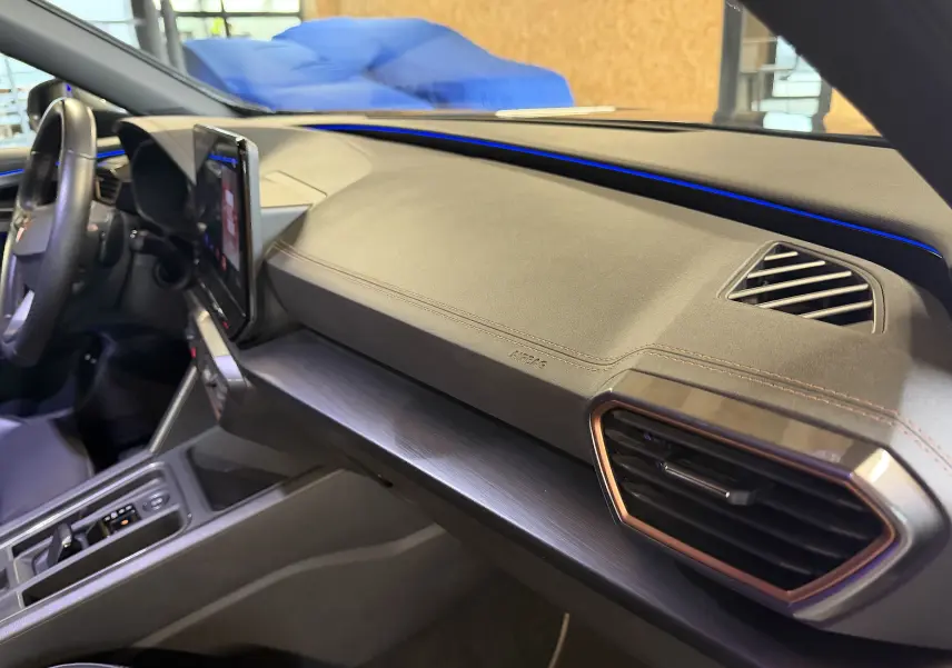 Vue intérieure côté passager du tableau de bord gris clair de la CUPRA Formentor 1.4 Hybrid 2023 avec éclairage bleu et aérateurs cuivrés.