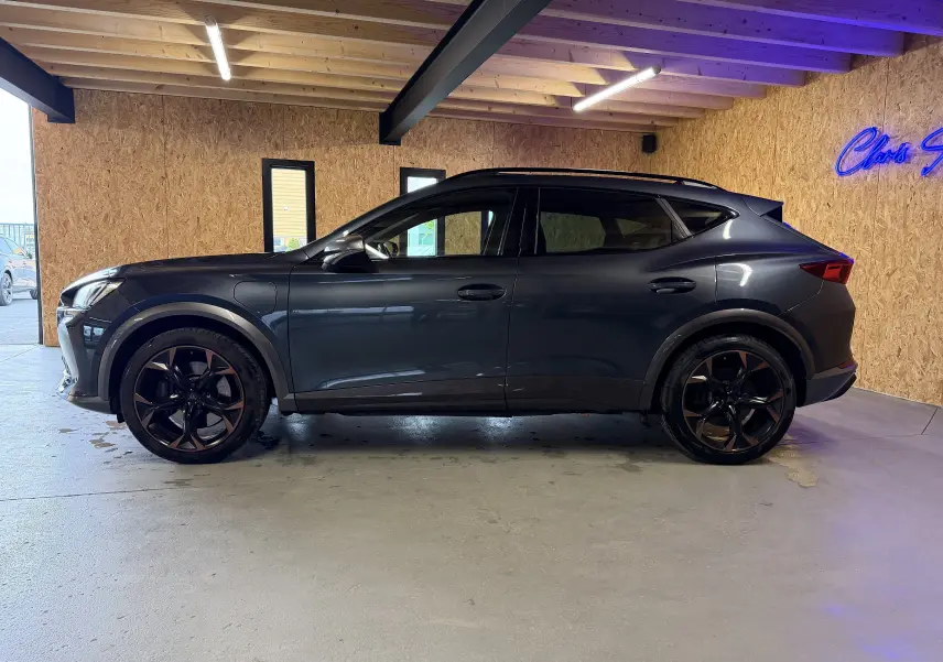 Vue de profil côté gauche d'une CUPRA Formentor gris clair avec jantes cuivrées dans un garage éclairé.