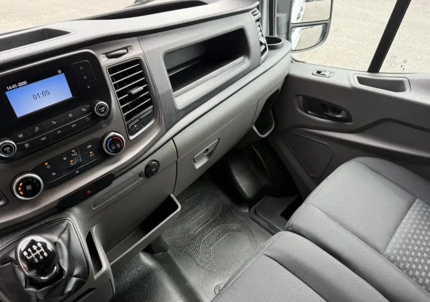 Vue intérieure côté passager du Ford Transit Fourgon 2024, tableau de bord gris et siège tissu gris.