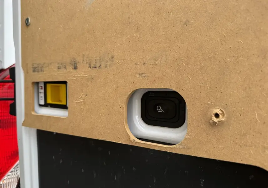 Gros plan sur un interrupteur intégré dans la cloison intérieure en bois du fourgon Ford Transit blanc, côté arrière gauche.
