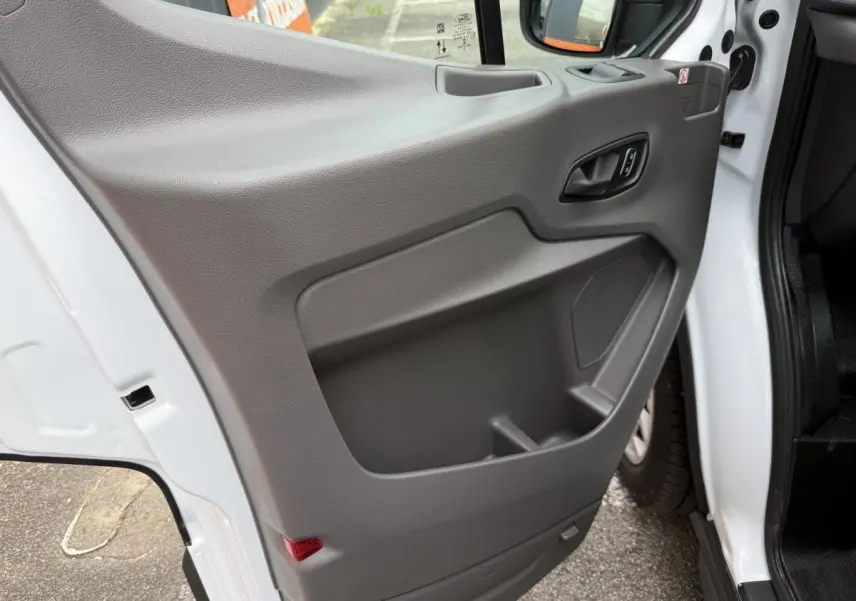 Vue rapprochée de la porte avant gauche grise du Ford Transit Fourgon blanc, montrant la poignée et le rangement intégré.