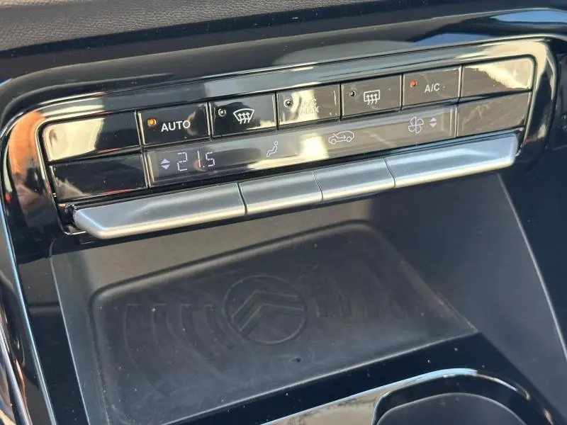 Vue rapprochée de la commande de climatisation automatique et du chargeur sans fil avec logo Citroën dans une C3 2025 Bright Blue.