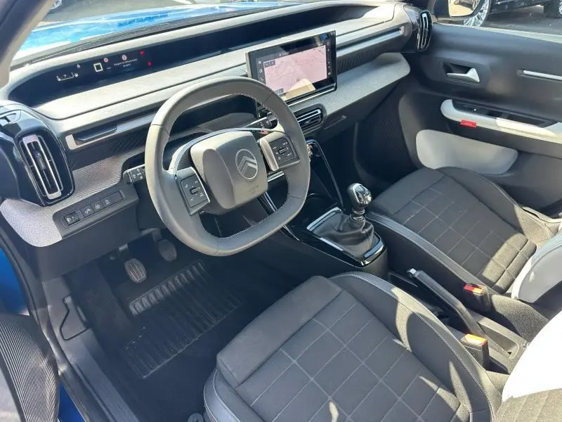 Vue intérieure côté conducteur de la Citroën C3 1.2 Turbo 2025, volant carré, sièges tissu noir et écran tactile central.