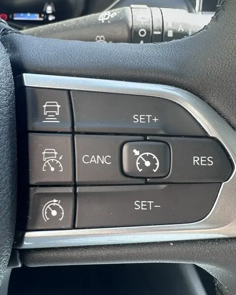 Gros plan sur les commandes du régulateur de vitesse au volant du Jeep Compass noir 2025, boutons noirs avec marquages blancs.