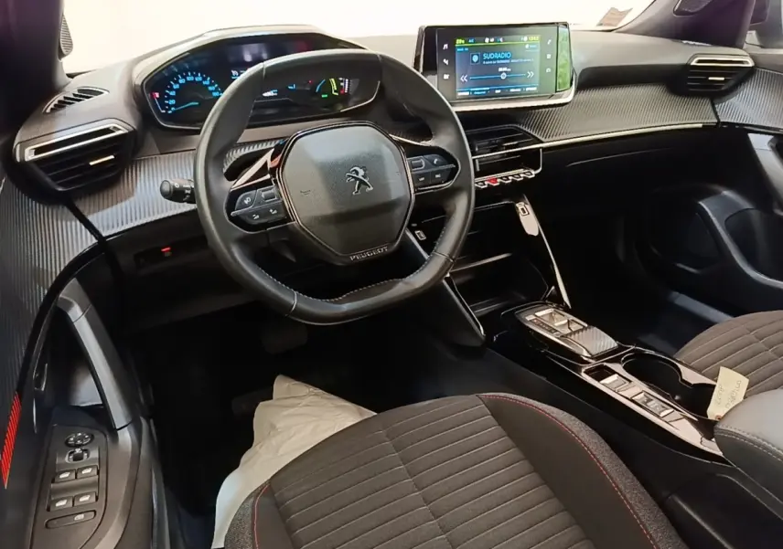 Vue intérieure avant droite du Peugeot E-2008 électrique gris clair, volant cuir et écran tactile central lumineux.