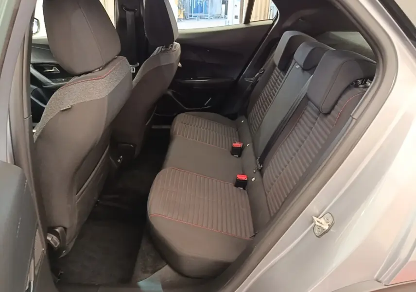 Vue côté gauche de l’habitacle arrière gris clair du Peugeot E-2008 électrique avec sièges tissu noir et surpiqûres rouges.