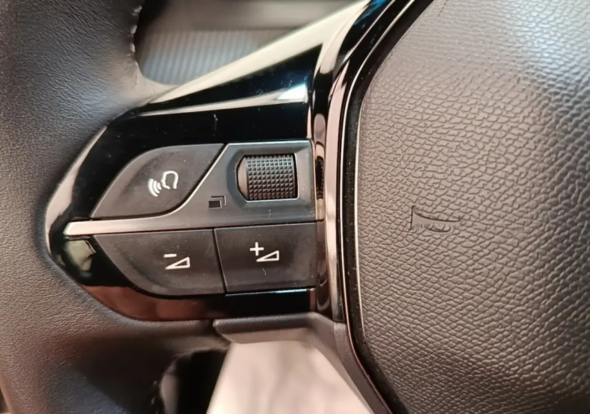 Gros plan sur les commandes gauche du volant cuir noir du Peugeot E-2008 électrique gris clair 2023.