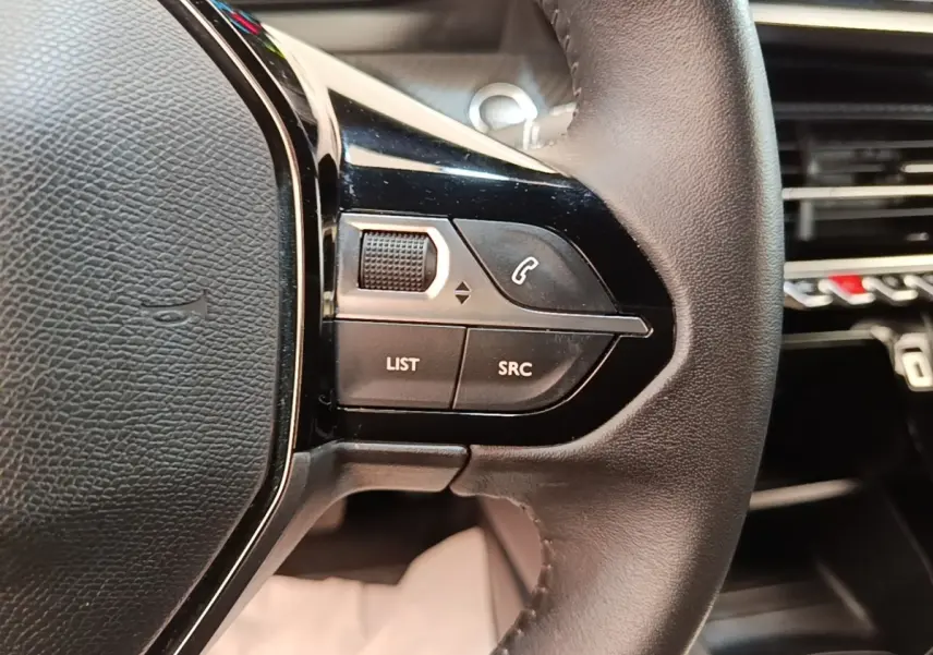 Gros plan sur la partie gauche du volant cuir noir du Peugeot E-2008 électrique, avec commandes intégrées.