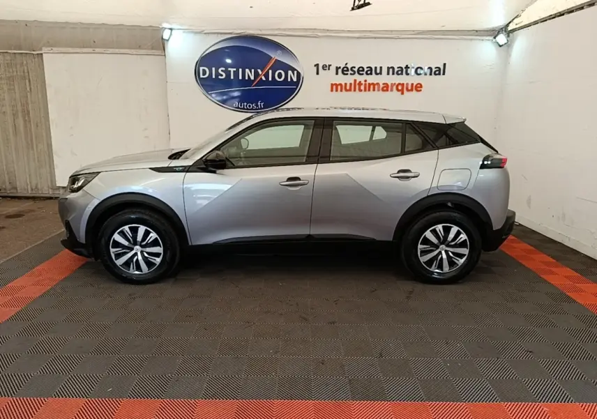 Profil côté gauche d’un Peugeot E-2008 électrique gris clair, avec jantes distinctives et toit noir en showroom.