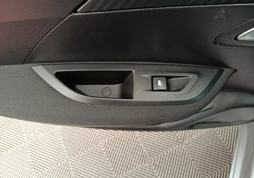 Gros plan sur la poignée intérieure et commande de lève-vitre côté droit d’un Peugeot E-2008 électrique gris clair.