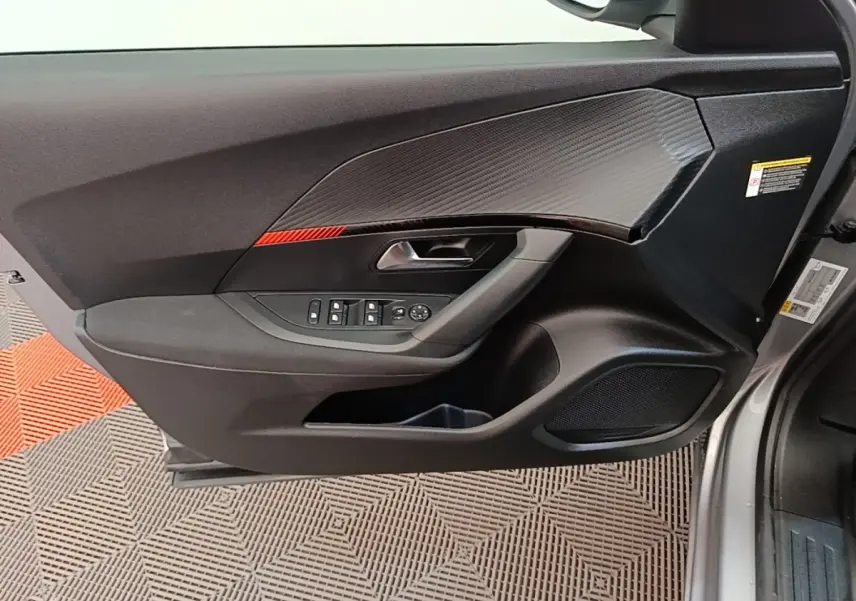 Vue intérieure côté gauche de la porte avant gris clair du Peugeot E-2008 électrique avec insert carbone et commandes fenêtres.