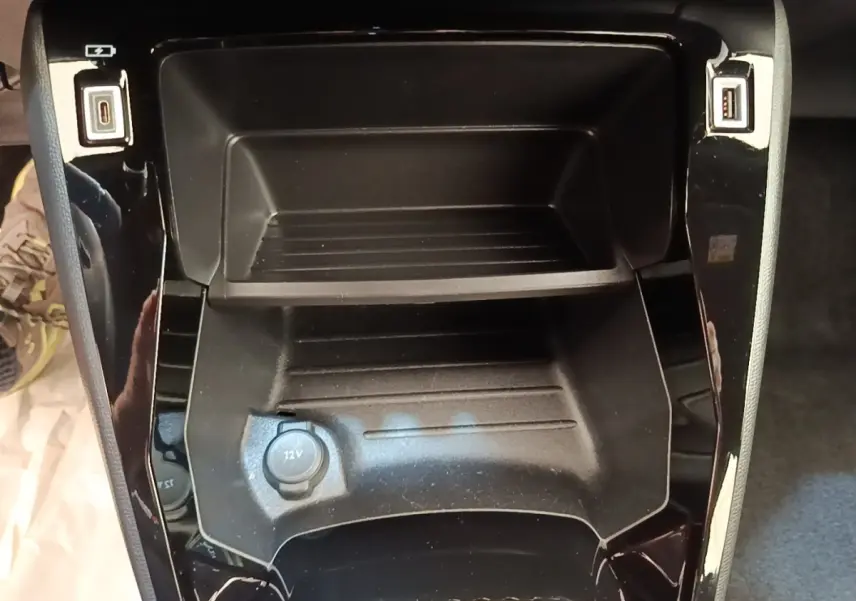 Vue rapprochée du rangement central noir avec prise 12V et ports USB du Peugeot E-2008 électrique gris clair.