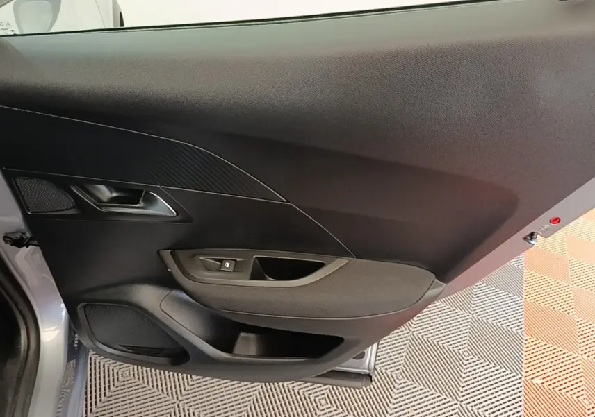 Vue rapprochée de la porte avant gauche gris clair du Peugeot E-2008 électrique avec poignée et commande de vitre.