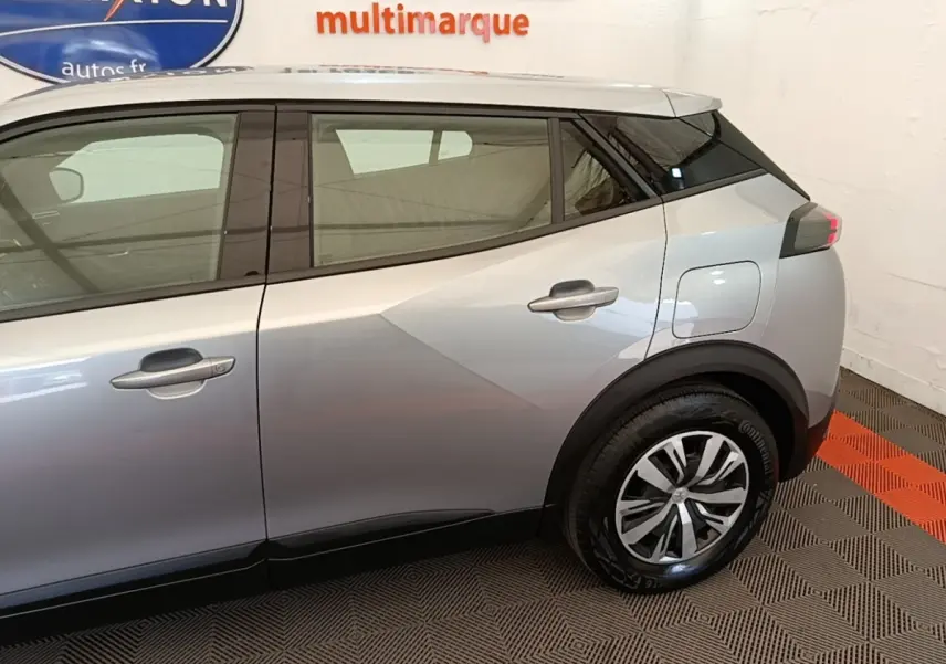 Vue latérale côté droit du Peugeot E-2008 électrique gris clair, mettant en valeur la porte arrière et la roue arrière.