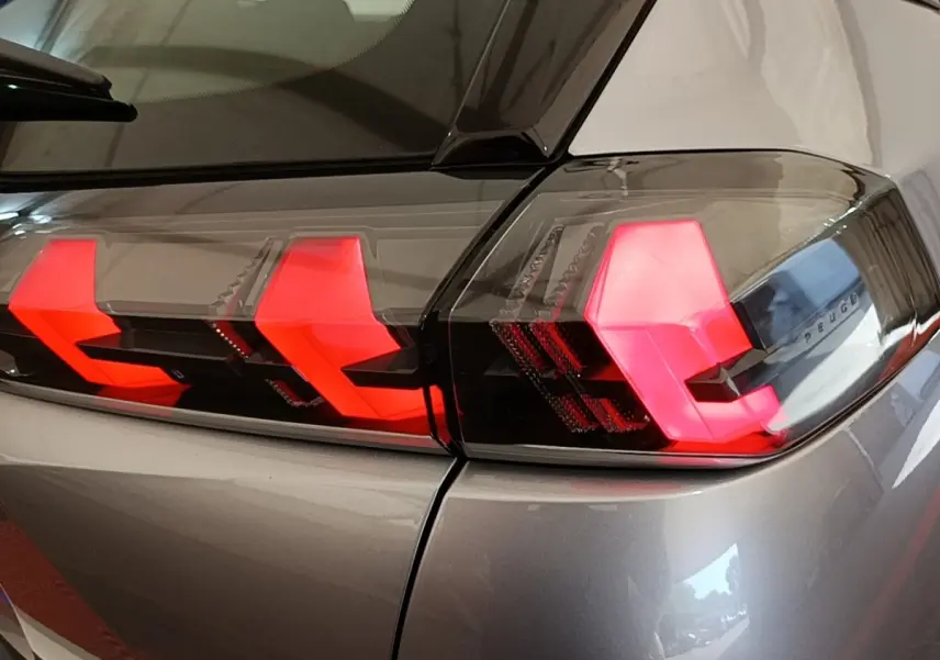 Gros plan sur les feux arrière allumés du Peugeot E-2008 électrique gris clair, vue côté droit arrière.