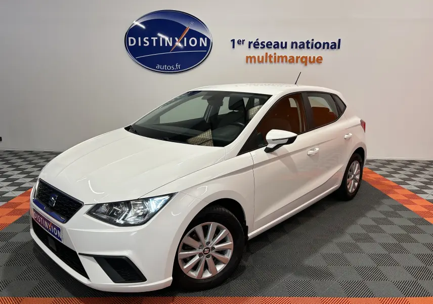 SEAT Ibiza blanc vue 3/4 avant droit en intérieur, avec phares allumés et jantes alliage simples.
