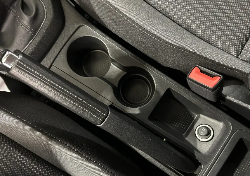 Gros plan sur la console centrale noire de la SEAT Ibiza 2019, avec frein à main, porte-gobelets et prise 12V visible.