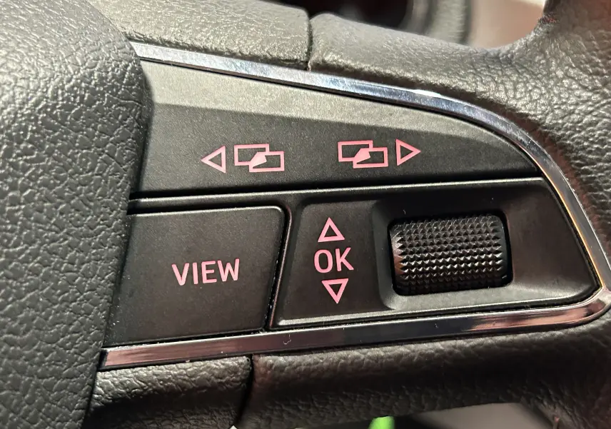 Gros plan sur les commandes du volant d'une SEAT Ibiza blanche 2019, boutons noirs avec inscriptions roses.