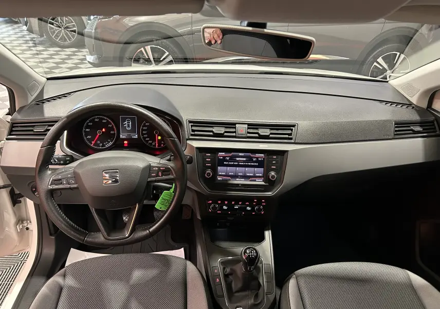 Vue intérieure frontale du tableau de bord et volant noir d'une SEAT Ibiza blanche 2019 avec boîte manuelle et sièges chauffants.