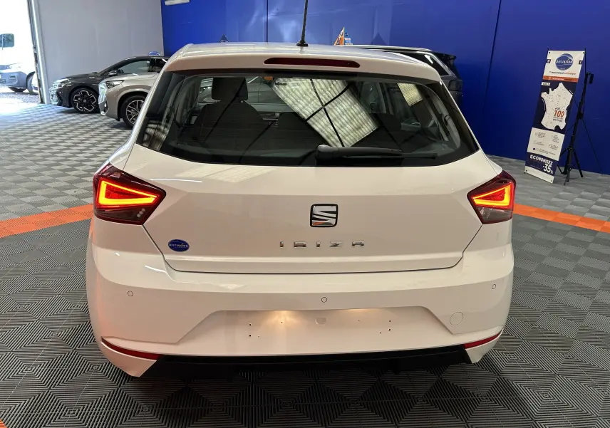 Vue arrière d'une SEAT Ibiza blanche de 2019 avec feux arrière allumés dans un showroom intérieur.