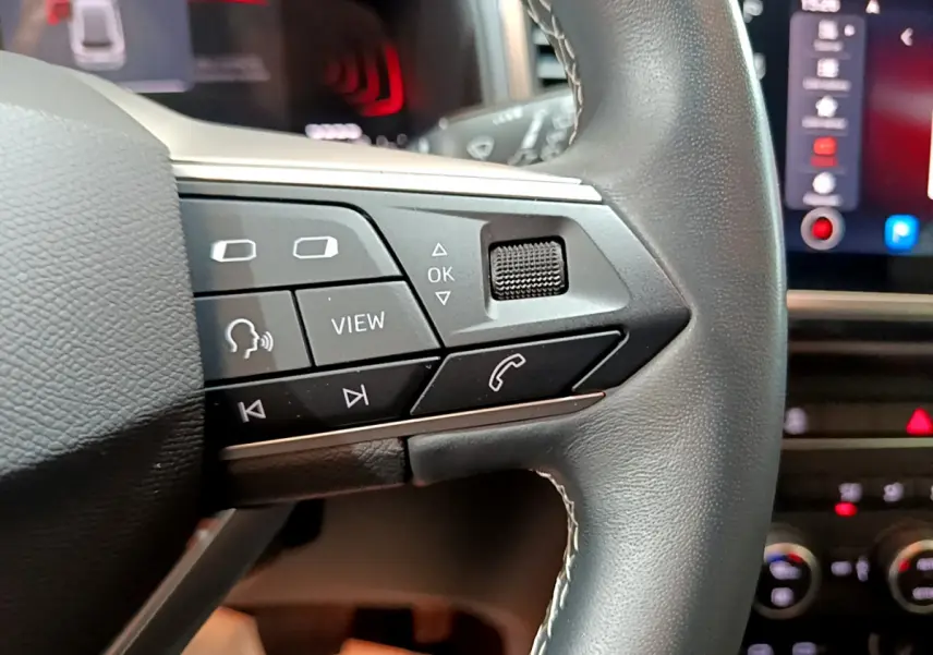 Gros plan sur les commandes du volant cuir noir du SEAT Ateca 2022, avec écran tactile et tableau de bord en arrière-plan.