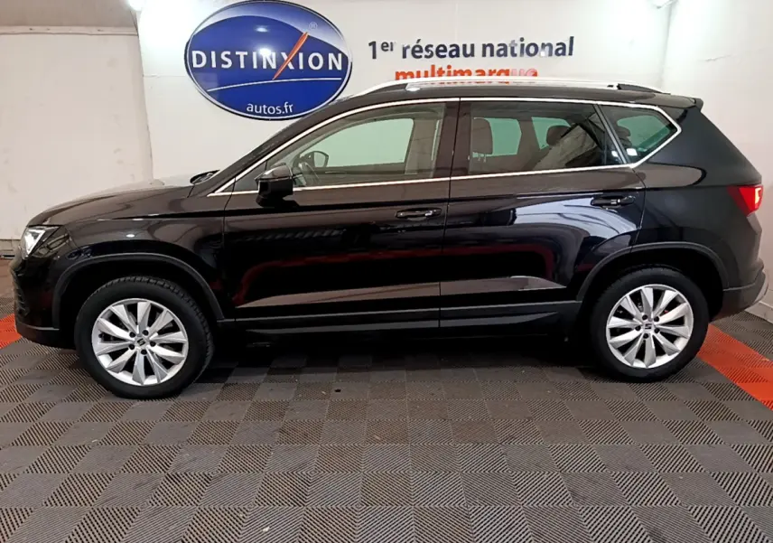 Profil côté gauche d'un SUV SEAT Ateca noir 2022 garé en intérieur avec jantes alliage et barres de toit chromées.