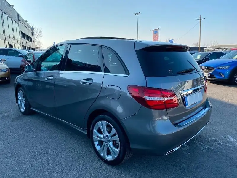 Vue 3/4 arrière droite d'une Mercedes Classe B 180 d gris foncé métal, avec jantes alliage et vitres teintées.