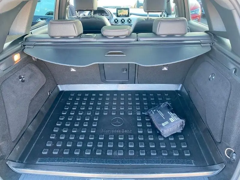 Coffre ouvert vu de l’arrière d’une Mercedes Classe B 180 d gris foncé métal avec tapis de coffre et cache-bagages.