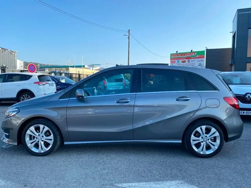 Vue de profil côté gauche d'une Mercedes Classe B 180 d 2016 gris foncé métallisé avec jantes alliage.