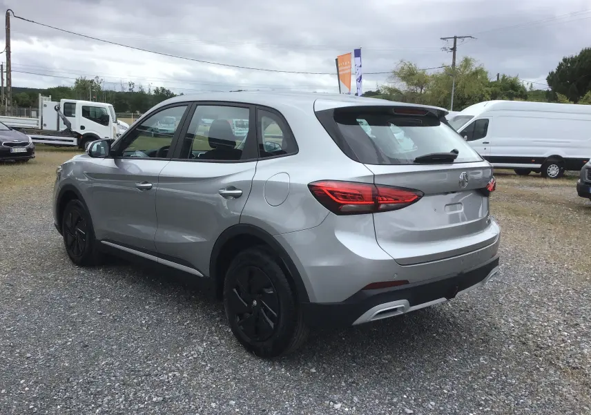 Vue 3/4 arrière droite du MG ZS Cosmic Silver avec feux arrière LED et jantes acier noires sur parking.