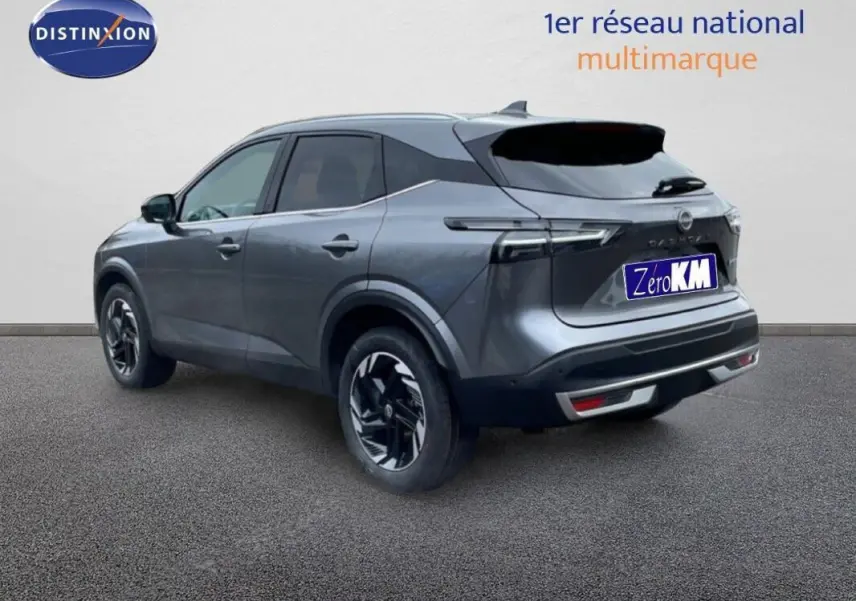 Vue 3/4 arrière droite d'un Nissan Qashqai gris 2025 avec barres de toit et jantes noires distinctives.