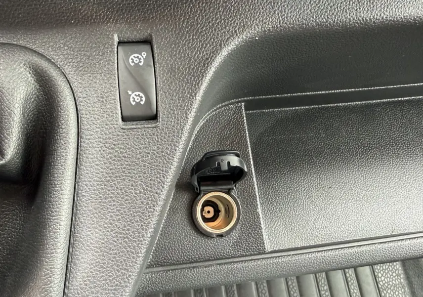 Gros plan sur la prise 12V ouverte et le bouton de régulateur de vitesse sur le tableau de bord noir du Renault Master blanc.