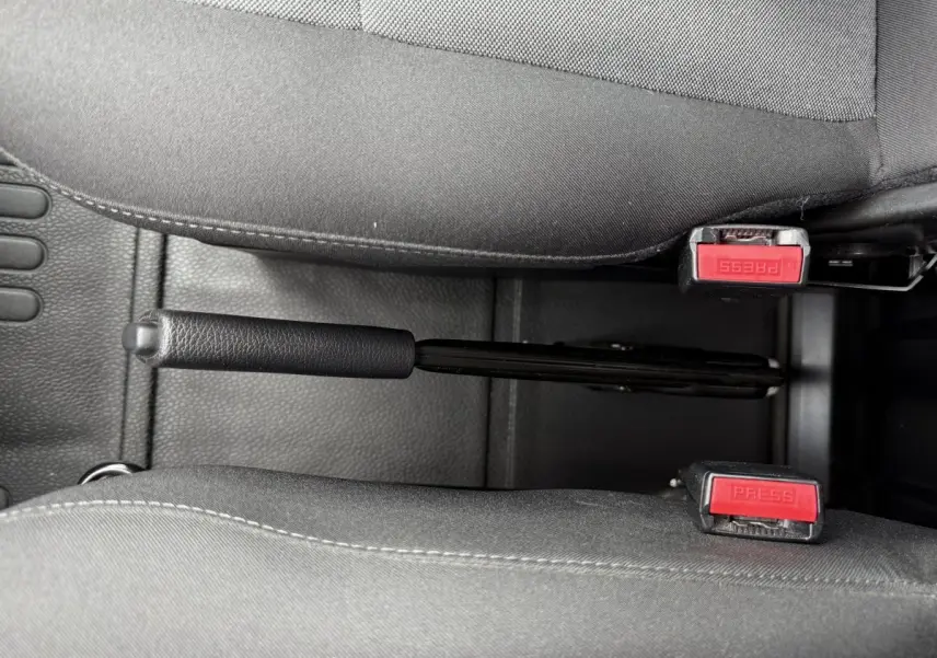 Vue rapprochée de la poignée de frein à main noire entre deux sièges gris dans l'habitacle du Renault Master blanc.