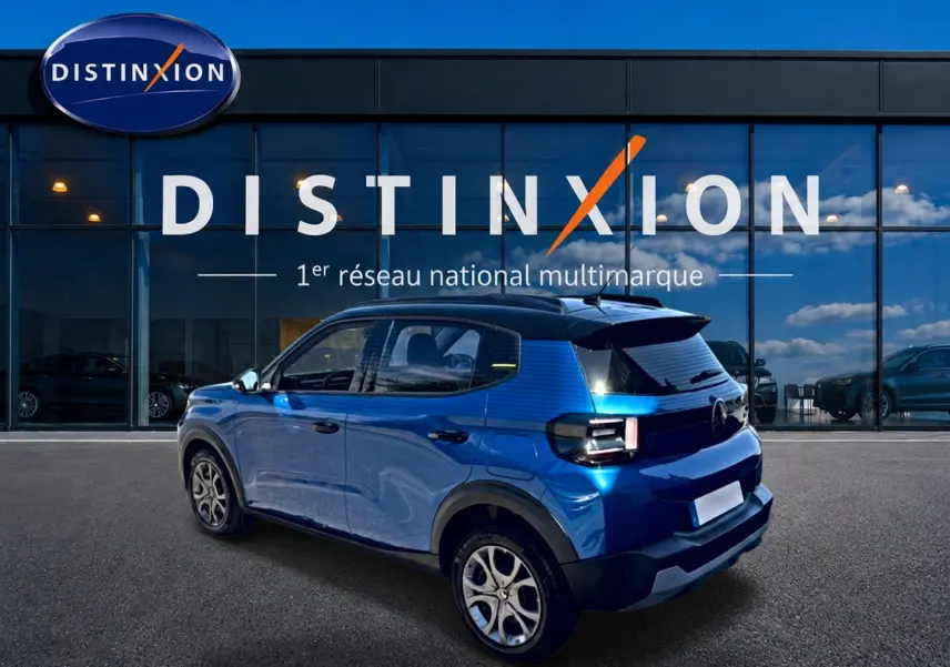 Vue 3/4 arrière droite d'une Citroën C3 2025 bleu avec toit noir et jantes alu devant une vitrine Distinxion.