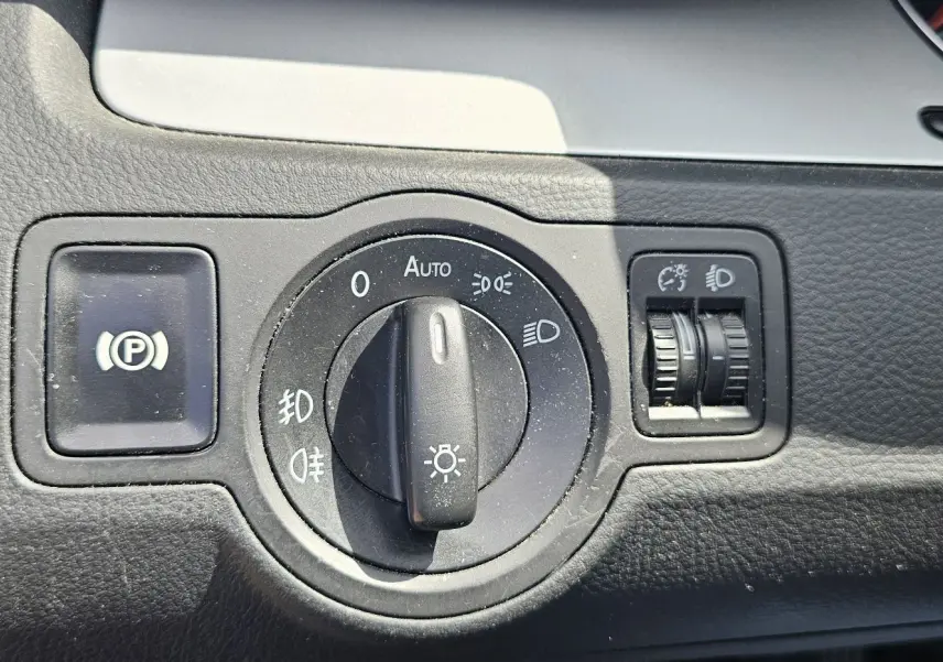 Gros plan sur le bouton de commande des phares et frein à main électrique dans une Volkswagen Passat bleu 2009.