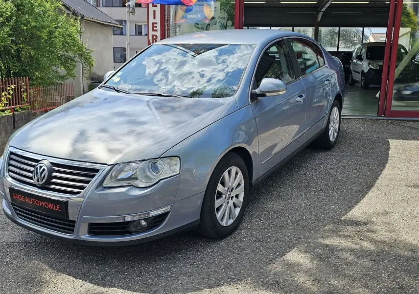 Volkswagen Passat 1.4 TSI bleu vue 3/4 avant droit, stationnée devant un garage avec plaque Sage Automobile.