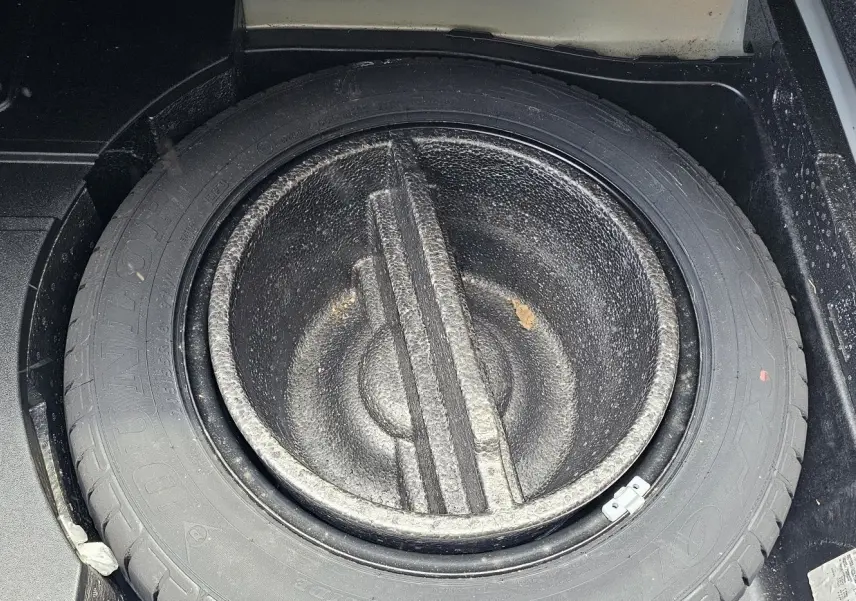 Gros plan sur la roue de secours et son logement dans le coffre d'une Volkswagen Passat bleue de 2009.