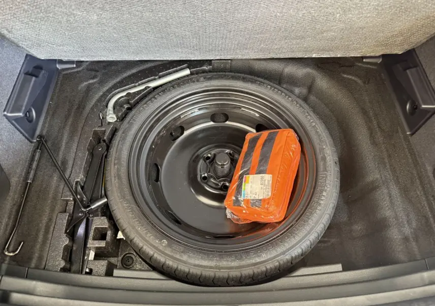 Vue plongeante sur la roue de secours noire et le kit de sécurité orange dans le coffre du SEAT Ateca gris clair.
